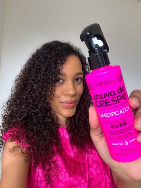 Mulher negra com cabelo cacheado definidos mostrando produto Umidificador Forever Liss Chuva de Crespo