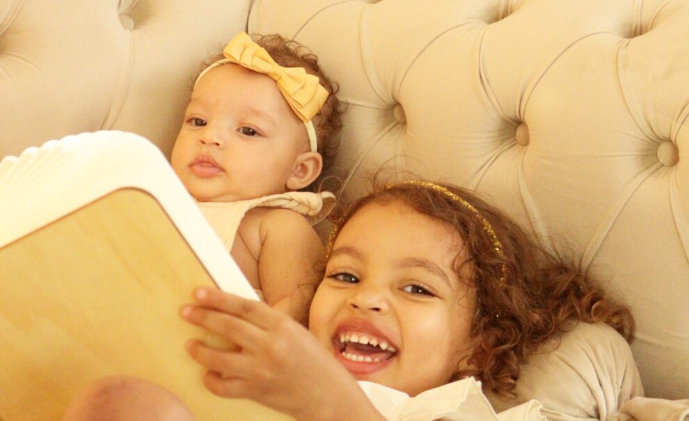 duas crianças vendo um livro. Um bebê de 6 meses e a outra tem três anos e está sorrindo