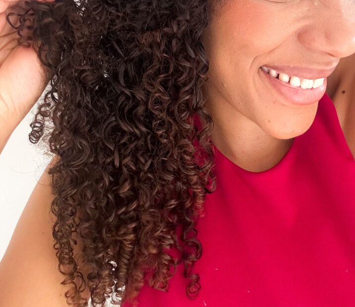 Mulher negra sorrindo mostrando os cabelos cacheados de perto. Ela usa cropped pink