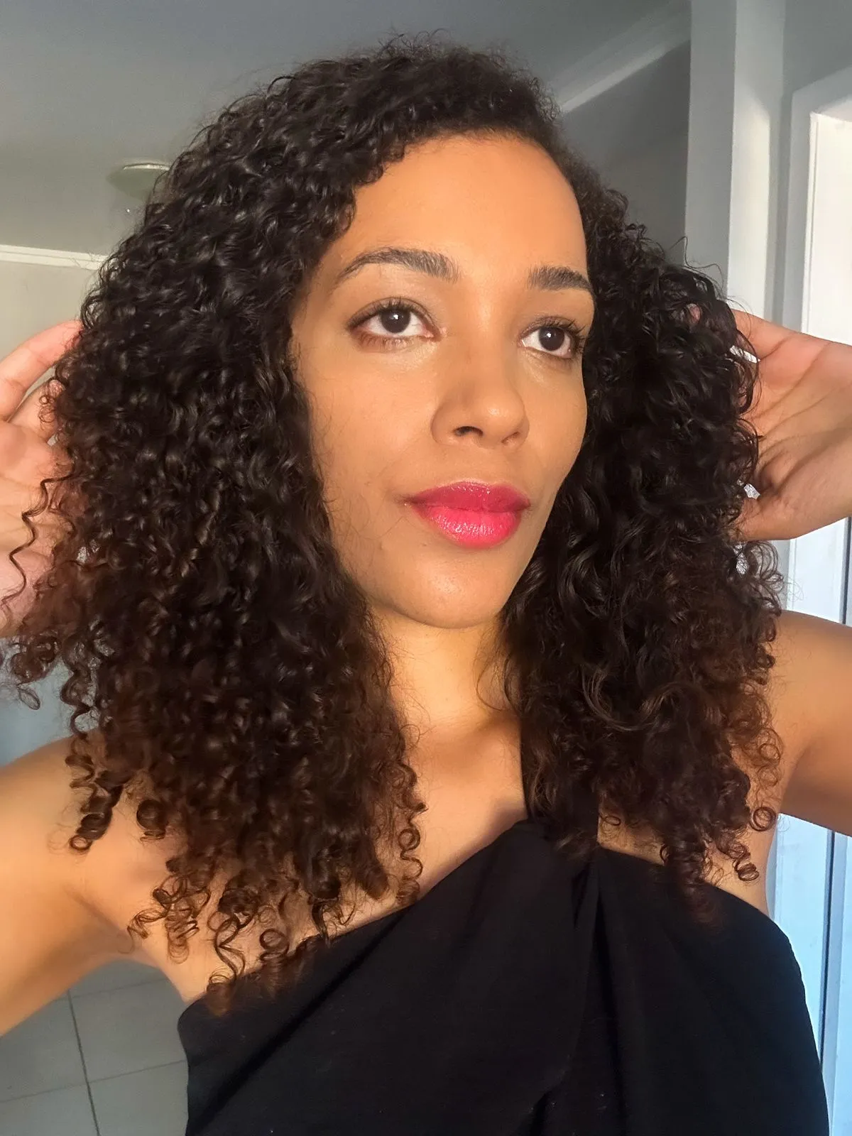 mulher negra com as mãos no cabelo cacheado mostrando resultado da máscara para cabelos secos natura lumina